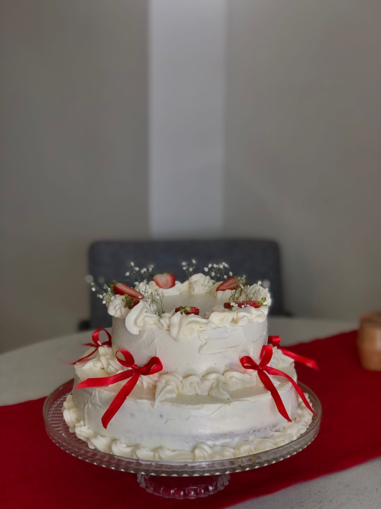 Kırmızı saten kurdeleler ve taze çileklerle süslenmiş iki katlı bembeyaz butik pasta